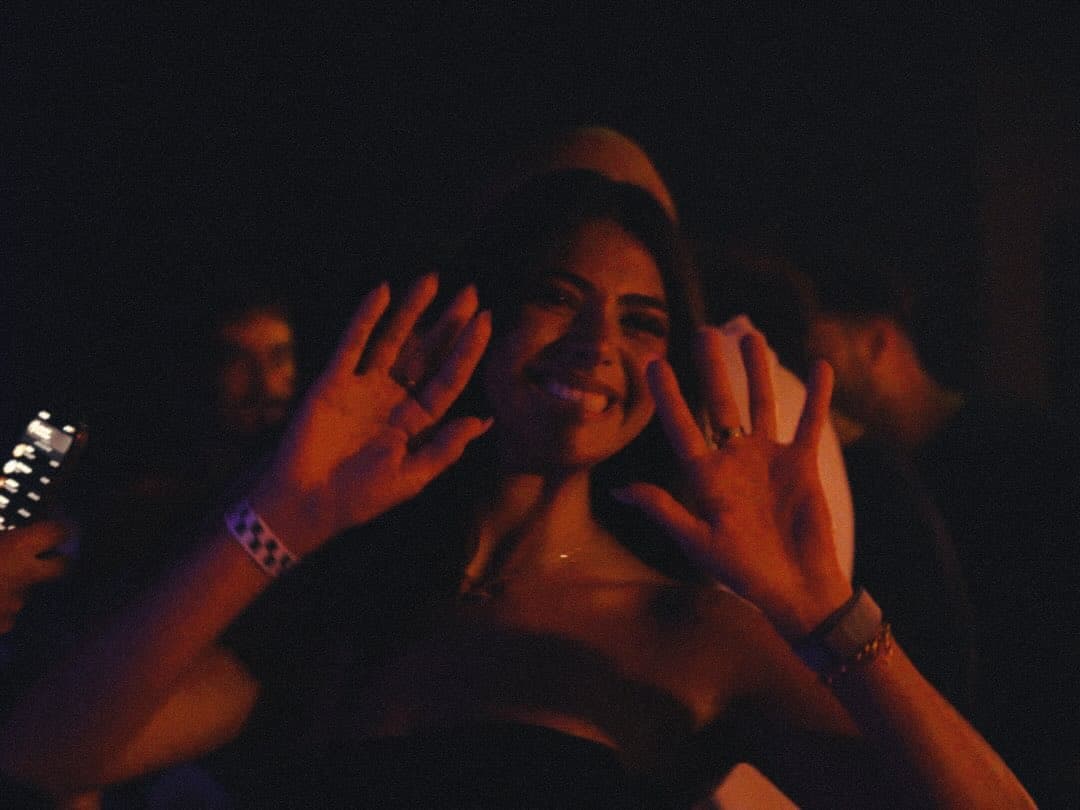A guest with both hands raised, lit red, in the dark at Lights Out