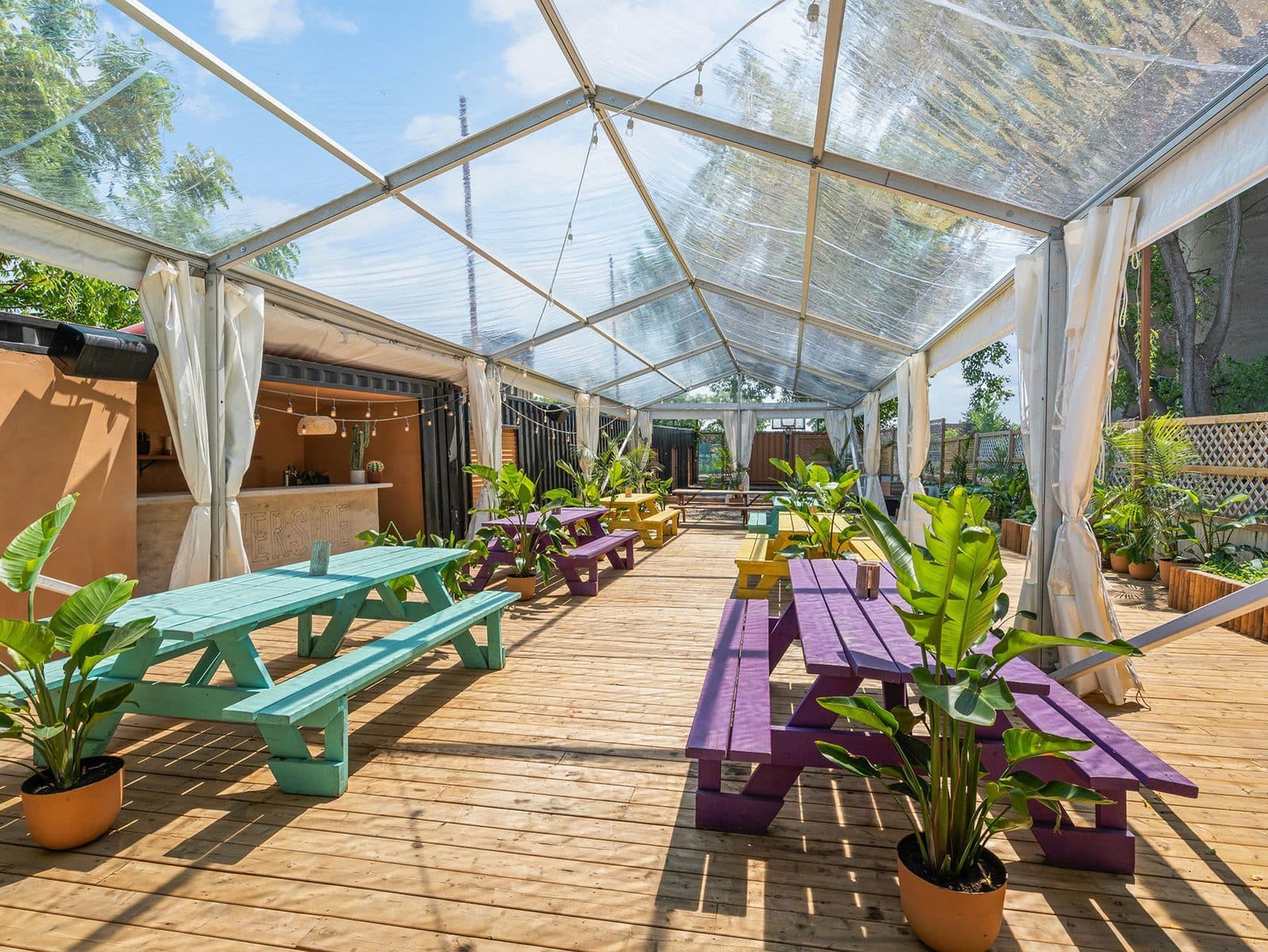 The marquee at Riverside St-Henri: long painted tables on a wooden deck under a clear roof